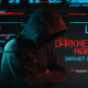 Vermummte Person ohne Gesicht vor dunklem Hintergrund mit farbigen Schriftzügen Darknet