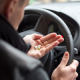 Mann am Steuer hält Tabletten in der Hand
