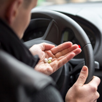Mann am Steuer hält Tabletten in der Hand
