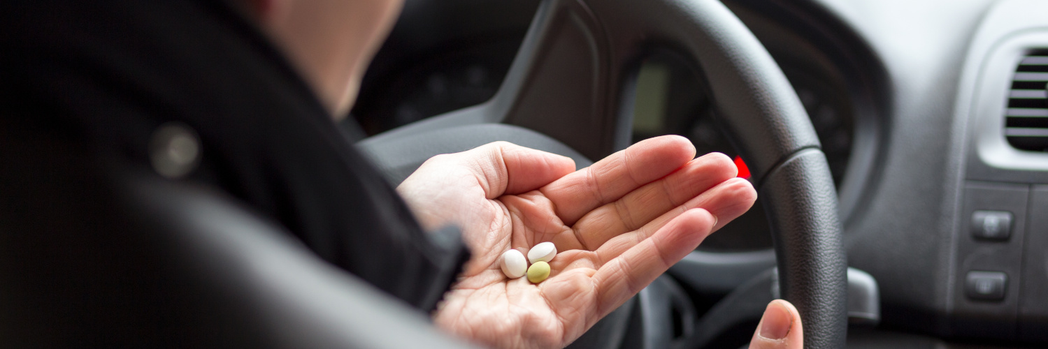 Mann am Steuer hält Tabletten in der Hand