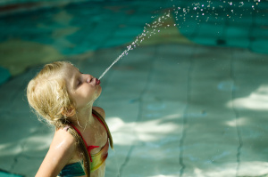 Kleines Kind spuckt im hohen Bogen Wasser ins Schwimmbecken