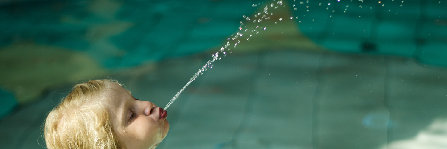 Kleines Kind spuckt im hohen Bogen Wasser ins Schwimmbecken
