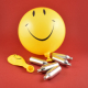 Lachgasflaschen mit gelbem Smileyballon vor rotem Hintergrund