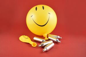 Lachgasflaschen mit gelbem Smileyballon vor rotem Hintergrund