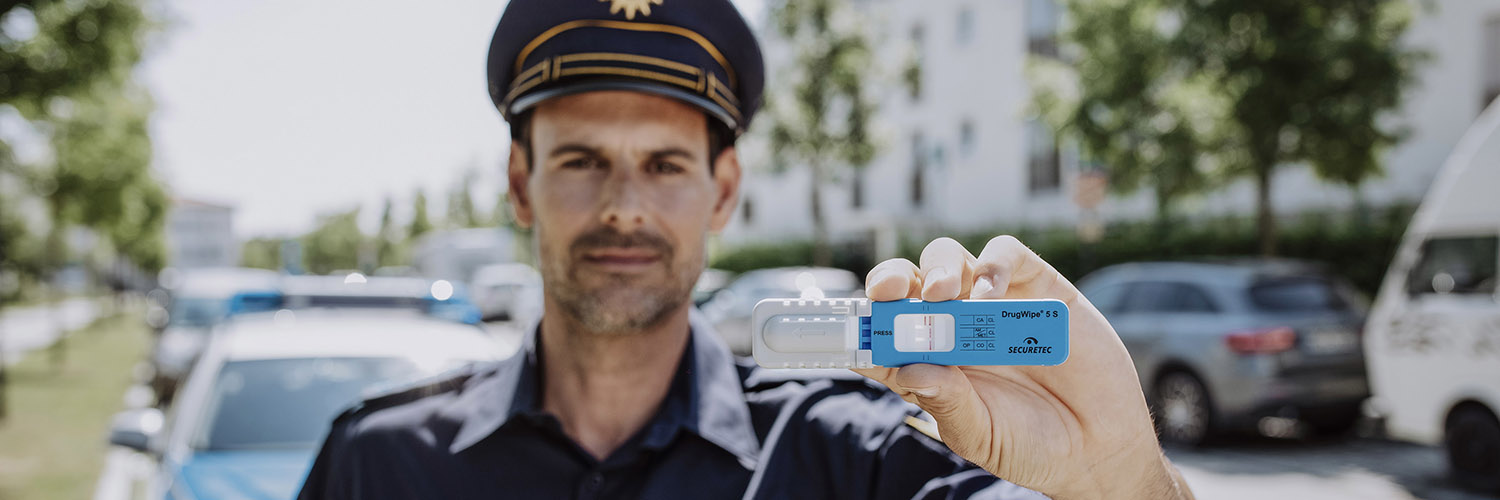 Ein Polizist hält den blau-weißen Drogenschnelltest DrugWipe vor die Kamera