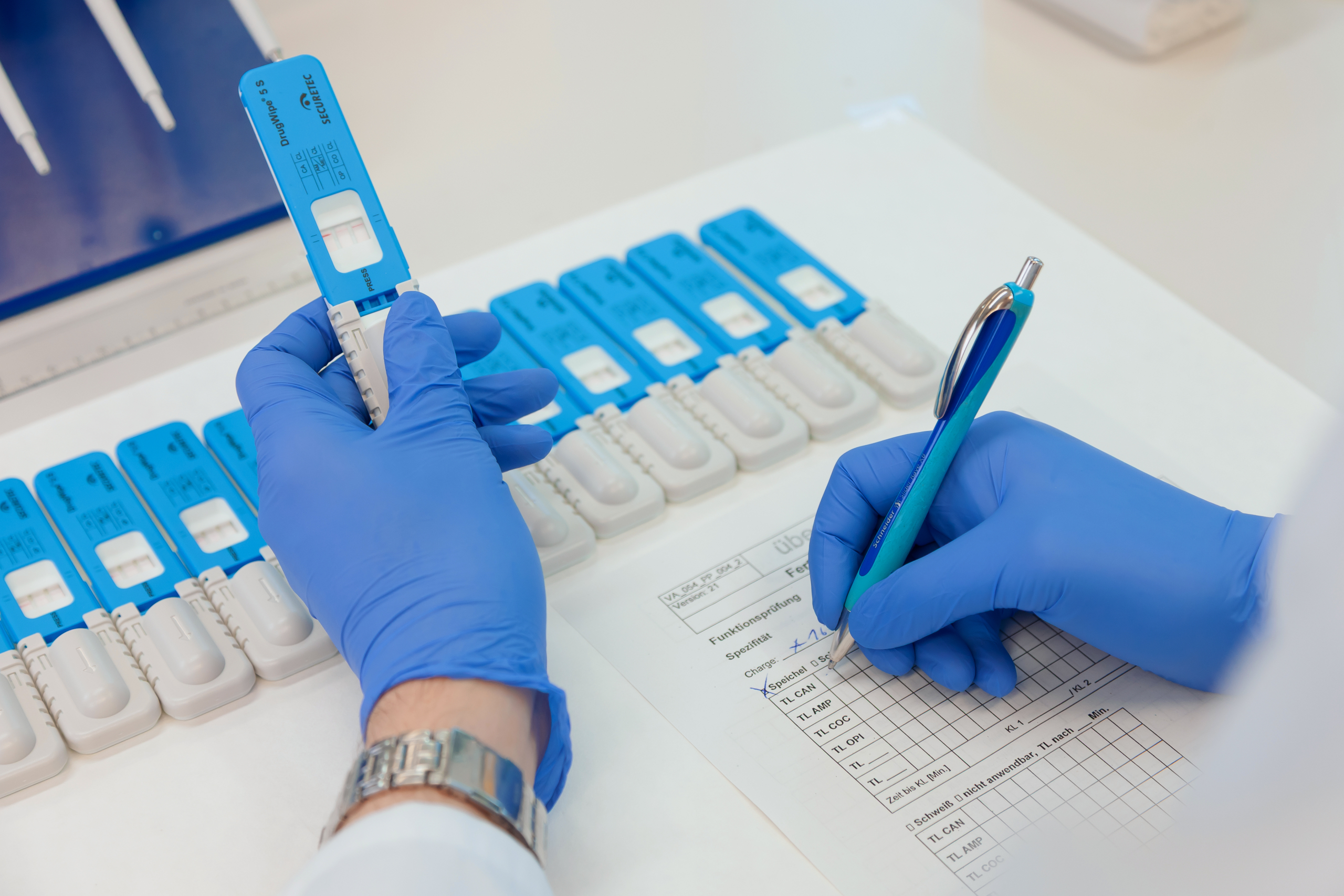 Mehrere DrugWipe Tests nebeneinander und eine Hand, die auf einem Zettel das Testergebnis festhält