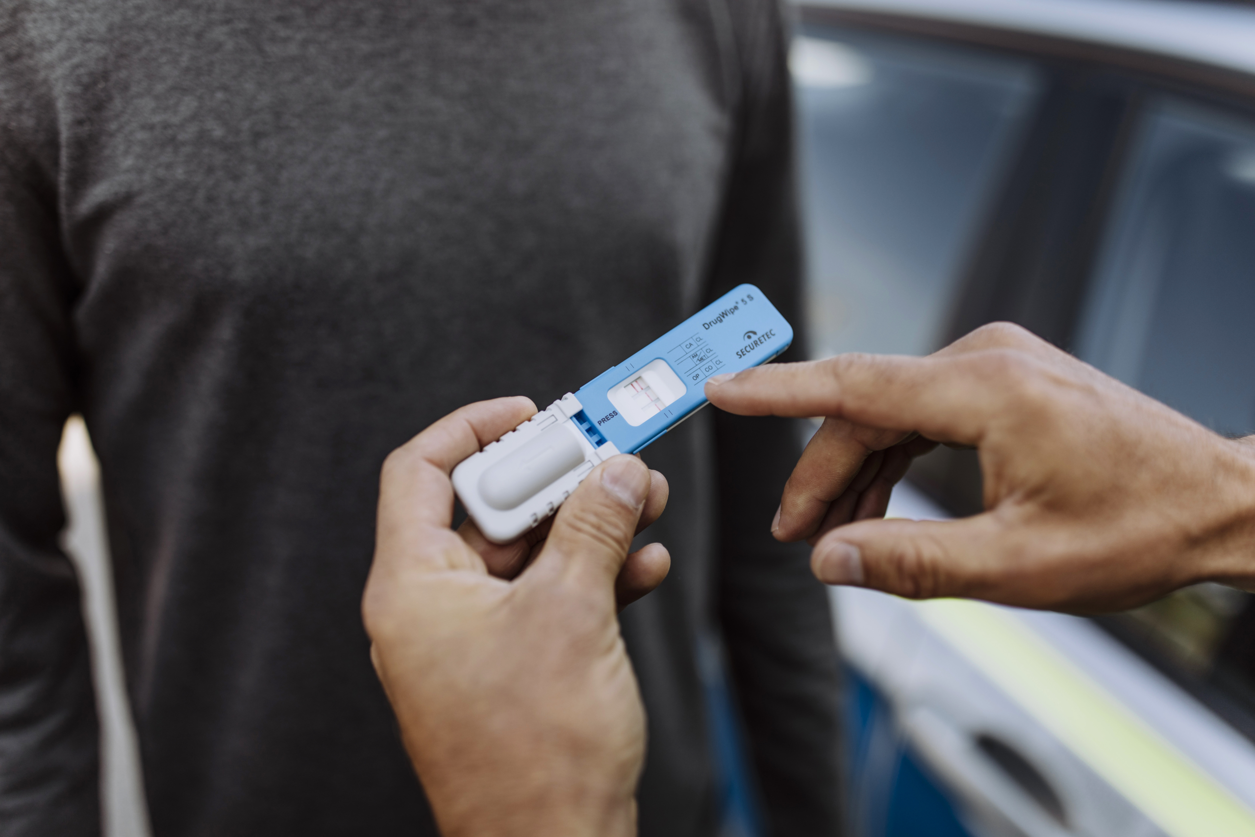 DrugWipe S 5 in der Hand, ein Finger zeigt auf das Testergebnis