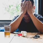 Mann mit Händen vor dem Gesicht, vor ihm liegen Tabletten auf einem Tisch