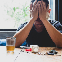 Mann mit Händen vor dem Gesicht, vor ihm liegen Tabletten auf einem Tisch