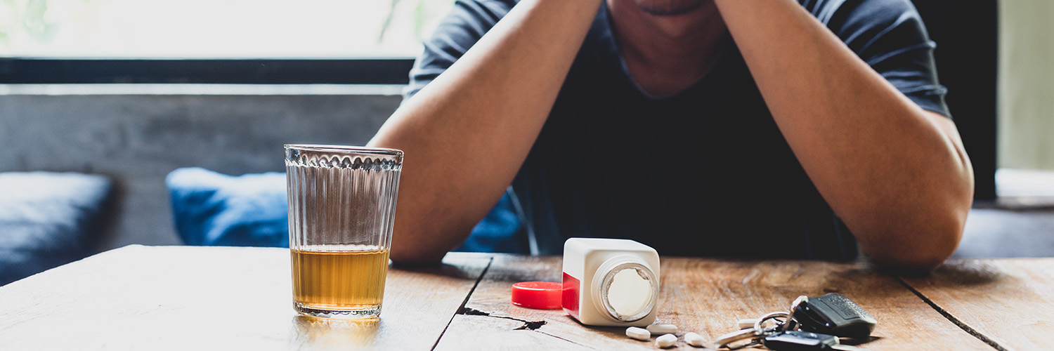Mann mit Händen vor dem Gesicht, vor ihm liegen Tabletten auf einem Tisch