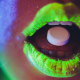 Geöffneter Mund teils in neon-gelb mit Pille auf Zunge