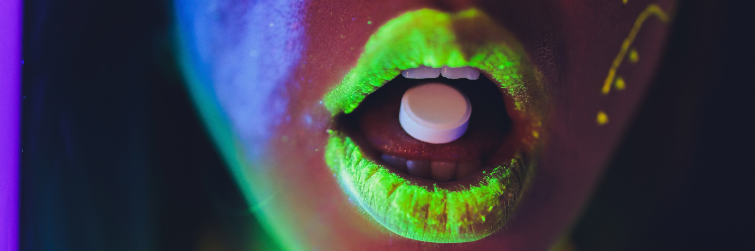 Geöffneter Mund teils in neon-gelb mit Pille auf Zunge