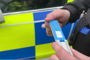Blau-weisser Drogenschnelltest DrugWipe wird vor einem Polizeiauto mit zwei Händen gehalten