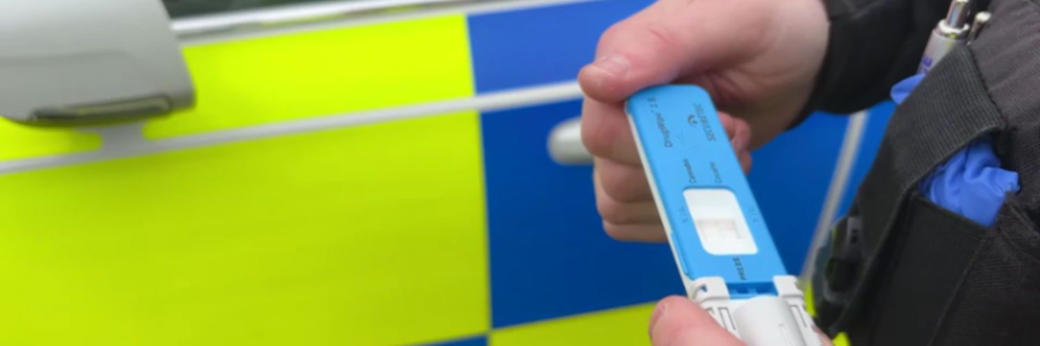 Blau-weisser Drogenschnelltest DrugWipe wird vor einem Polizeiauto mit zwei Händen gehalten